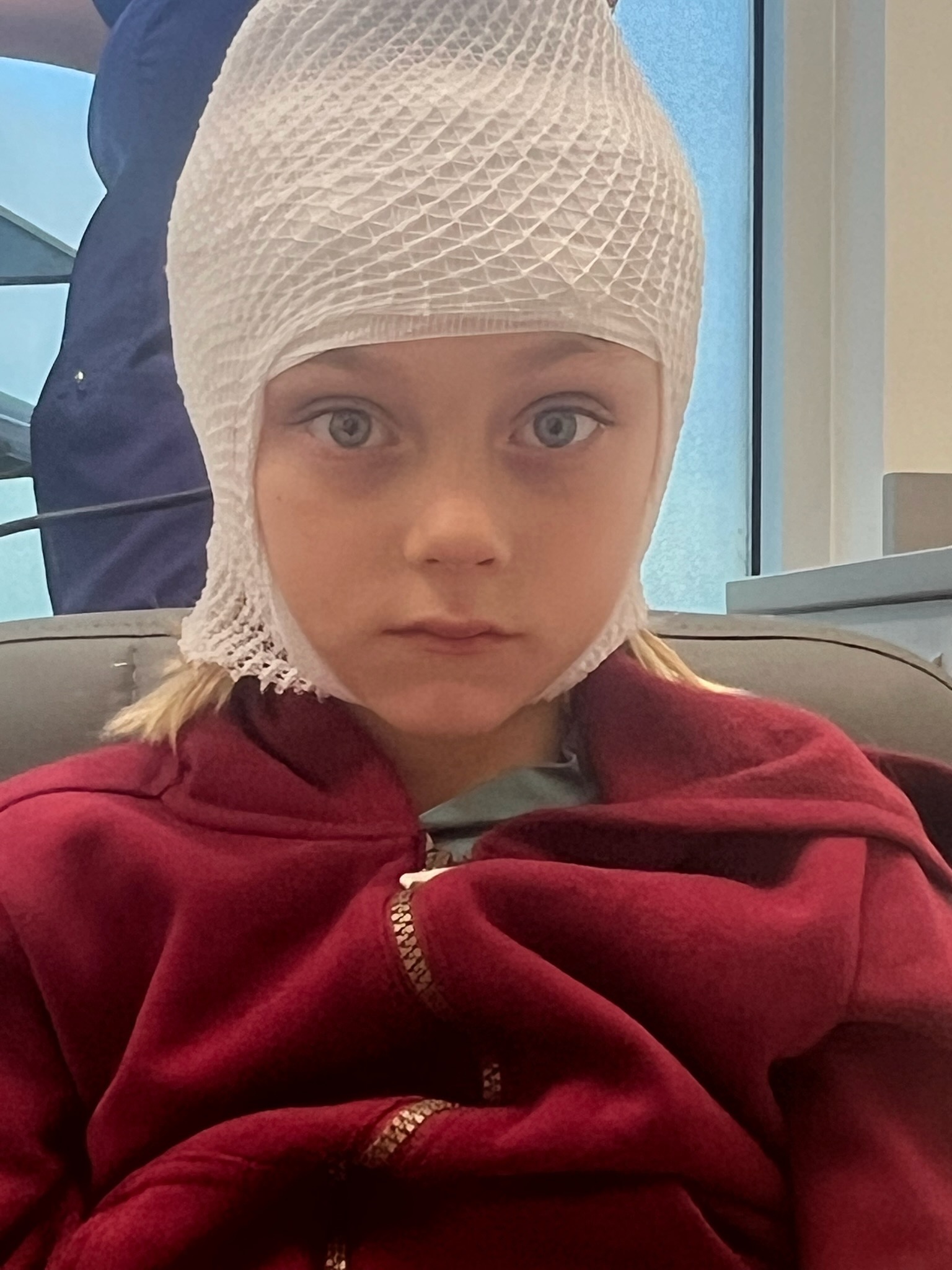 Elijah at eight years old, wearing an EEG mesh cap and red hoodie, looking directly at the camera